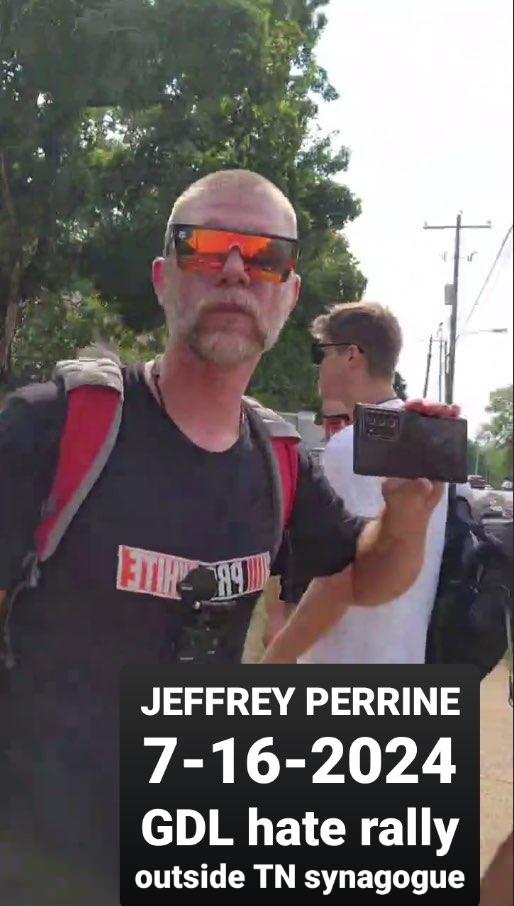 White man and his beard is outside in the sun with reflective sunglasses over his eyes. He is holding up a phone to record. Picture label reads, "Jeffrey Perrine 7-16-2024 GDL hate rally outside Tennessee synagogue."