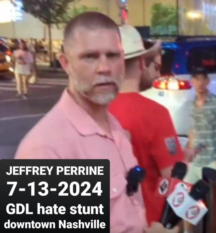 A white middle-aged man with short hair and beard that has patches of graying hair. He is wearing a summery button-down shirt. It is night time and he is with several men on a city street. He has two microphones in his hand and a go-pro camera on his chest. A picture label reads, "Jeffrey Perrine 7-13-2024 GDL hate stunt downtown Nashville."