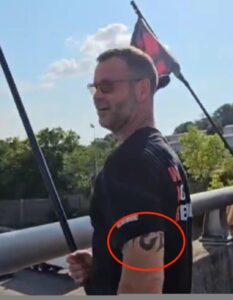 michael lee francis holding a flag on an overpass in nashville with his tattoo sticking out from his short sleeve tee looking like a tool